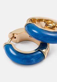 Blå harpiks hoopsøreringer med gullfargede metallaksenter. Sirkulært design med jevn tekstur og glanset overflate. Merkevaren logo synlig på innsiden.