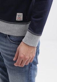 Felpa navy con polsini e orlo grigi, con un piccolo etichetta con scritto "Athletic Dept." Morbido al tatto e dalla vestibilità casual.