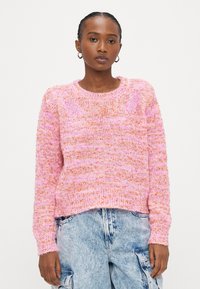 Rozā adīts džemperis ar teksturētu rakstu, apaļu izgriezumu un garām piedurknēm. Valdīts virs gaiši zilām, vaļīgām džinsa cargo biksēm.