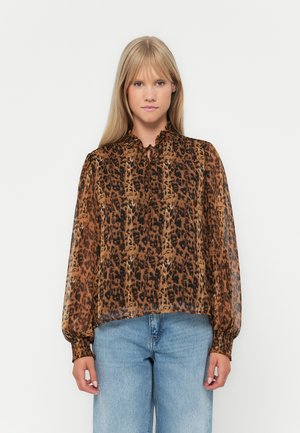Gjennomsiktig brun bluse med svart leopardmønster, høy volangkrage og elastiske mansjetter. Sammenlignet med lyseblå bukser med løs passform.