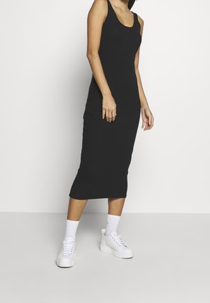 Robe midi noire sans manches avec une coupe ajustée, fabriquée en tissu lisse, associée à des baskets à plateforme blanches et des chaussettes blanches côtelées.