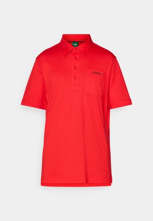Rdeča polo majica iz gladkega materiala, z ovratnikom, kratkimi rokavi in žepom na levi strani prsnega dela, okrašenim z logotipom.