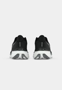 Une paire de chaussures de course noires et blanches vues de l'arrière, montrant des semelles rembourrées avec des motifs de bande de roulement gris.