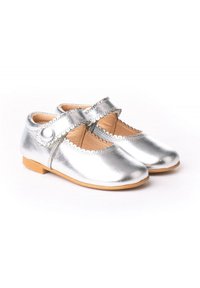 Zapatos Mary Jane metálicos plateados con un diseño en forma de onda, suela plana y cierre a presión, que cuentan con plantillas color tostado y una textura suave.