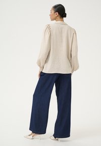 Beige gestreepte blouse met pofmouwen en elastische manchetten, gecombineerd met een wijde donkerblauwe denim broek en witte hakken.