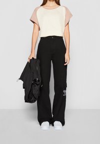 Svarta cargobyxor med sidofickor, ihopparade med en topp med raglanärmar i krämfärg och rosa. En svart lättviktsjacka hänger över armen.