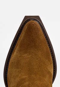 Chaussure en daim marron à bout pointu avec un liseré cousu marron foncé et un bord de semelle empilée.