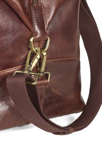 Bruine leren tas met een gestructureerde afwerking, voorzien van bronzen hardware, een stoffen schouderband en gedetailleerde stiksels langs de randen.