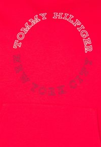 Red hoodie featuring circular white and navy text: "TOMMY HILFIGER" at the top and "NEW YORK CITY" at the bottom. Cotton material.