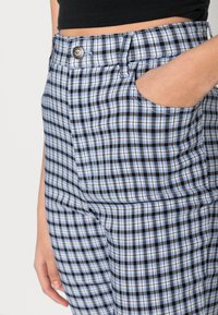 Calças azul e preta em padrão xadrez, feitas de um tecido com uma textura suave. Apresentam um bolso frontal e um botão metálico na faixa da cintura.