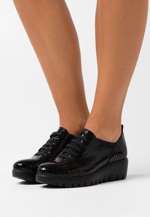 Des chaussures noires à lacets avec un motif de serpent texturé et brillant. Semelle noire épaisse avec des détails striés. Bout arrondi et design de faible hauteur.