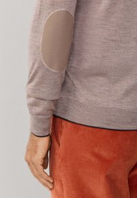 Beige trui met gebreid lijf en elleboogpatches. De trui heeft een ronde halslijn en geribde boorden. Gecombineerd met gestructureerde roestkleurige corduroy broek.