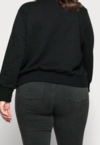 Zwarte sweatshirt met een geribde zoom en boorden, gecombineerd met donkergrijze jeans met achterzakken en een gladde textuur.