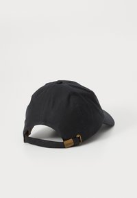 Boné de beisebol preto deitado, exibindo a alça ajustável com fivela de latão gravada "Barbour" em fundo branco.