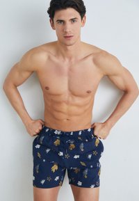 Námorné plavky s elastickým pásom s farebným kvetinovým a hviezdicovým vzorom v bielej, zlatej a modrej farbe.