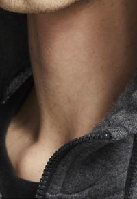 Grå zip-up hoodie med en texturerad tyg, som visar en närbild av kragen och nacken och framhäver sömmen och blixtlåsets detaljer.