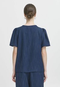 Navyblauw t-shirt met korte mouwen en subtiele verticale strepen, heeft een ronde halslijn en bolle mouwen. Gemaakt van een lichte, gestructureerde stof.