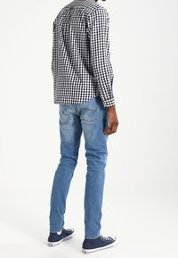 Black and white checkered long-sleeve shirt and light blue denim jeans, paired with dark blue sneakers, viewed from the back.