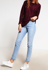 Burgundyröd långärmad tröja i kombination med ljusblå tajta jeans och vita sneakers, vilket visar en avslappnad passform och mjuk textur.