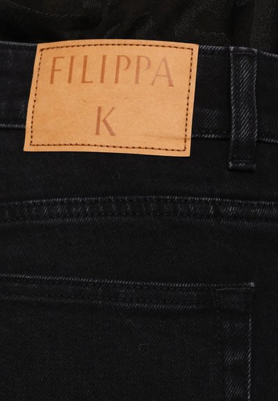 Jeans de mezclilla negra con una etiqueta de cuero que presenta el texto en relieve "FILIPPA K." Superficie texturizada, detalles de costura sutiles y un diseño clásico.