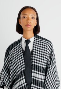 Čierno-biely károvaný šál s voľným strihom, s vzormi houndstooth a károvaných. Doplněný čiernym viazaním a bielou košeľou.