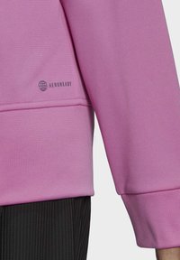 Sweatshirt rose avec une finition texturée, comportant un logo AEROREADY visible. Le design inclut un poignet large et une coupe décontractée.