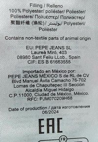 Etikett av vitt tyg med svart och färgad text. Innehåller en lista över material, skötselråd, producentinformation och produktionsdatum, formaterad på flera språk.