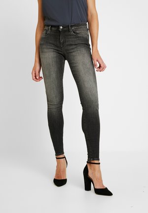 Jeans ajustados en denim gris degradado, con cintura de altura media, bolsillos frontales, acabado descolorido y costuras detalladas. Combinados con tacones negros.