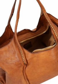 Tan leren tote bag met studs langs de zijkanten, een ritssluiting aan de bovenkant en een ruim interieur met een gevoerd vak.