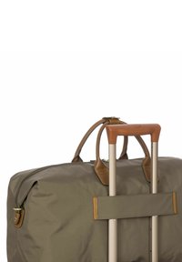 Sac de sport vert olive fabriqué en tissu durable, avec des accents en cuir et une poignée en métal rétractable. Il est doté d'une fermeture éclair et de détails cousus.