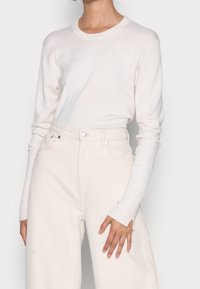 Chemise à manches longues crème clair en tissu doux, associée à un jean crème taille haute avec poche latérale et texture subtile.