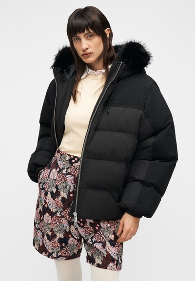 Μαύρο μπουφάν τύπου puffer με κουκούλα, διακοσμημένη με τεχνητό γούνινο περίγραμμα, με φερμουάρ και καπιτονέ σχέδιο, συνδυασμένο με σορτς με φλοράλ μοτίβο.