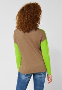 Brun och fluorescerande grön långärmad topp med rund halsringning och kontrasterande ärmar. Mjuk textur med en avslappnad passform.