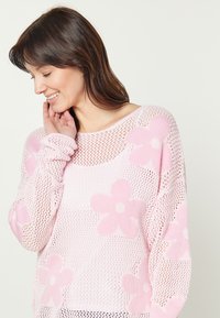 Maglione rosa lavorato a maglia con grandi motivi floreali, caratterizzato da un design a rete larga e scollatura ampia. Tessuto testurizzato con maniche lunghe.