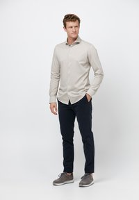 Lichtbeige lange mouw knoopshirt met een gladde textuur, gecombineerd met donkerblauwe broek en grijze sportschoenen. Eenvoudig, modern ontwerp.