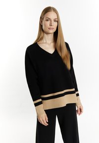 Maglione nero a maglia con scollo a V, caratterizzato da un orlo e dei polsini a strisce beige. Il tessuto sembra morbido con una consistenza liscia.