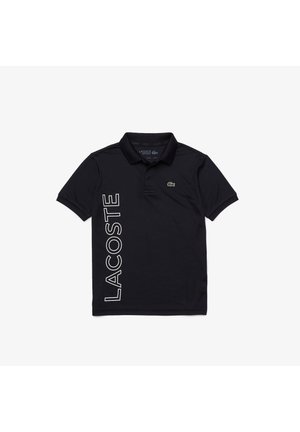 Polo negro de manga corta con cuello, texto vertical "LACOSTE" en el lado izquierdo y pequeño logo de cocodrilo verde en el pecho.