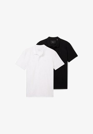 Fekete galléros póló, fekete rövidnadrággal párosítva. Az öltözéket fehér részletek díszítik a zoknikon és a vászoncipőkön. Egyszerű dizájn, minta nélkül.