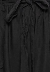 Black linen garment with a tied waistband, featuring a relaxed fit and subtle texture. It has side seams and is unadorned, focusing on simplicity.