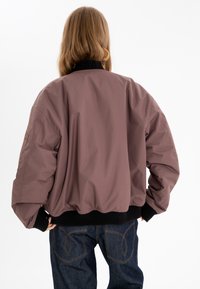 Bomberjacka i ljuslila med svart ribbad krage och manschetter, med en lös passform och mjuk textur. Bakifrån syns en elastisk nederkant.