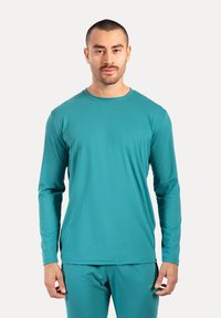 Langarm T-Shirt mit Rundhalsausschnitt in Teal, aus glattem, leichtem Stoff gefertigt. Es hat einen entspannten Schnitt mit dezenten Nahtdetails.