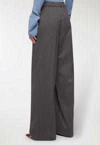 Spodnie o szerokich nogawkach w ciemnoszarym materiale, z elastycznym pasem i subtelną teksturą, z bocznymi rozcięciami dla większej swobody ruchów.