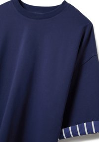 Camiseta de algodón azul marino con cuello redondo y mangas cortas; el patrón a rayas en las mangas añade contraste. Textura suave.