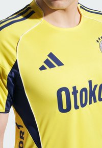 Žltý športový dres s námorníckymi modrými akcentmi, s okrúhlym výstrihom, logom Adidas a textom "Otokor1" v tučnom modrom písmene.