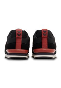 Czarne buty sportowe z czerwonym akcentem na pięcie, teksturowana cholewka oraz biała i szara podeszwa z wzorem trzymającym.