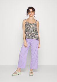 Top de alças finas preto com padrão floral, combinado com calças largas lilás e sandálias plataforma verdes. Textura suave e cores vibrantes.