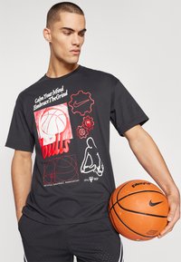 Camiseta de algodón negra con estampados gráficos en rojo y blanco, que incluyen un balón de baloncesto y la palabra "bulls". Combinada con pantalones cortos negros y un balón de baloncesto.