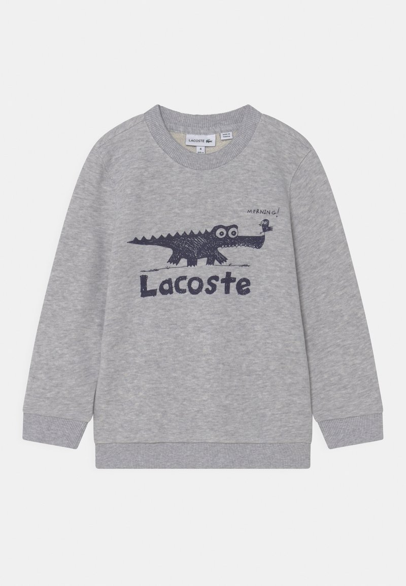 Sweat-shirt gris clair à manches longues avec poignets côtelés, présentant un crocodile noir caricatural et un oiseau avec le texte "Morning!" et le logo "Lacoste".