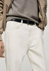 Pantaloni in cordura bianchi con una superficie testurizzata, dotati di un taglio classico, tasche laterali e una cintura in pelle nera indossata sopra un maglione grigio.