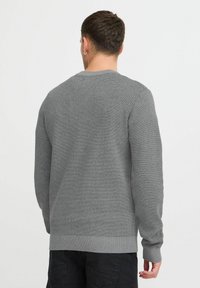 Maglione grigio a maglia con maniche lunghe, polsini e fondo a coste, caratterizzato da un tessuto testurizzato e un classico scollo rotondo.